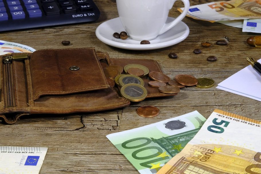 Ein offenes Portemonnaie mit Münzen und Geldscheinen auf einem Tisch, umgeben von Kaffeetassen.